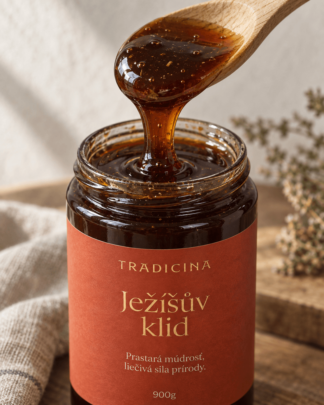 Detail drevenej lyžičky, z ktorej steká hustý tmavý med s bylinkami späť do otvoreného pohára Ježíšův klid