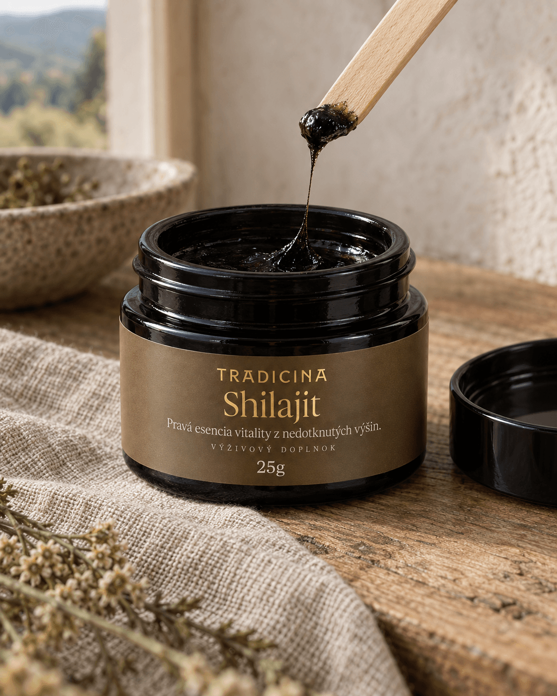 Detail čiernej shilajitovej živice, ktorá sa ťahá v tenkom vlákne z drevenej lyžičky do otvorenej dózy Shilajit TRADICINA 25 g